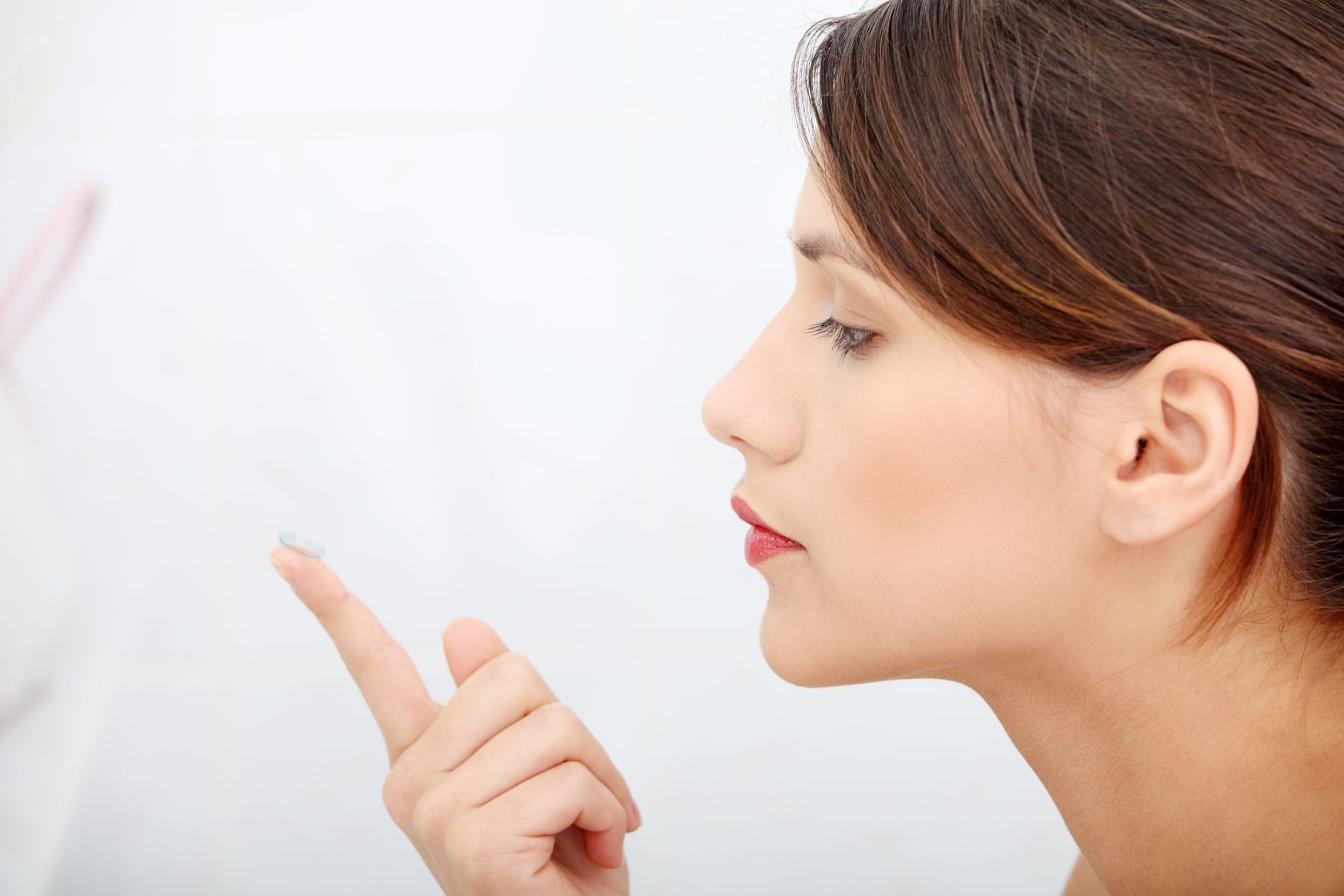 Mulher olhando para uma lentes de contato anuais sobre o dedo||Troca de lente de contato||